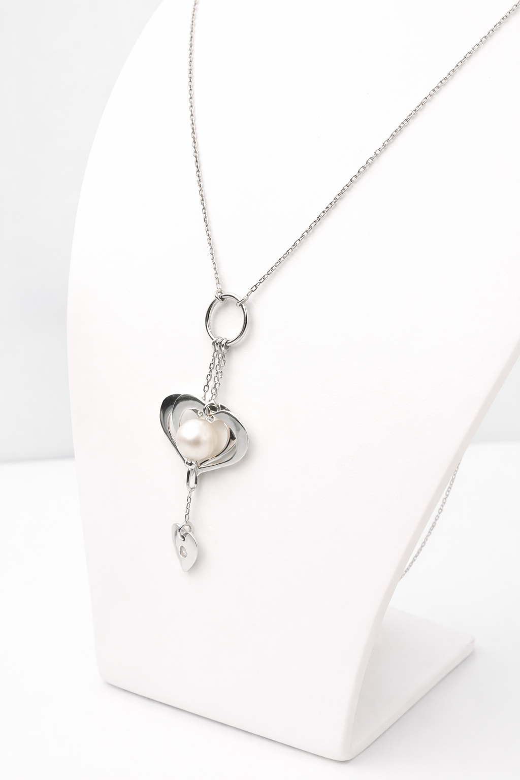 Collier en or blanc 18 carats avec pendentif perle et cœurs présenté sur un buste blanc.