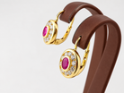 Boucles d'oreilles ovales en or jaune 18 carats présentées sur support marron, avec pierres roses et blanches.