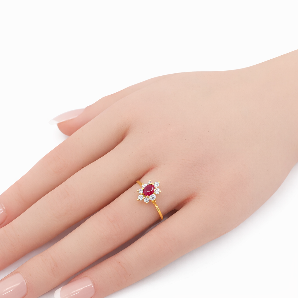 Main portant une bague en or jaune 18 carats sertie d’un rubis ovale entouré d’oxydes de zirconium
