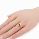 Main portant une bague en or jaune 18 carats sertie d’un rubis ovale entouré d’oxydes de zirconium